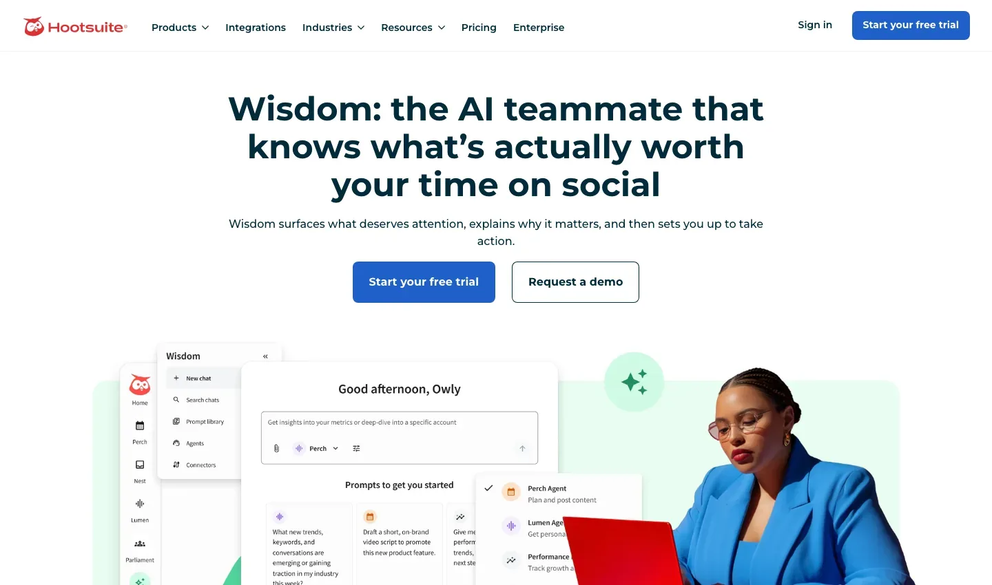 Hootsuite Wisdom homepage with a headline about an AI teammate for social media, free-trial and demo buttons, and a product mockup beside a person using a red laptop.